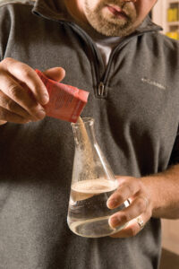 person pouring malt extract in to a beaker of water